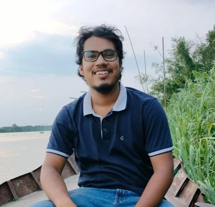 A man in a blue shirt stands with arms crossed, representing Hridoy CS, Graphic Designer at Rankupper.